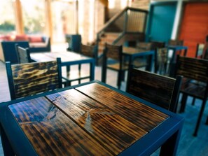 Interior de un restaurante con mesas y sillas de madera, una escalera al fondo y vistas al exterior.