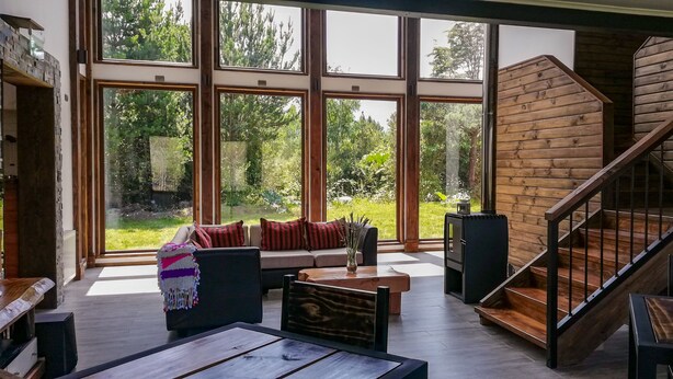 Un interior moderno con ventanas amplias, una escalera de madera y una zona de estar acogedora.