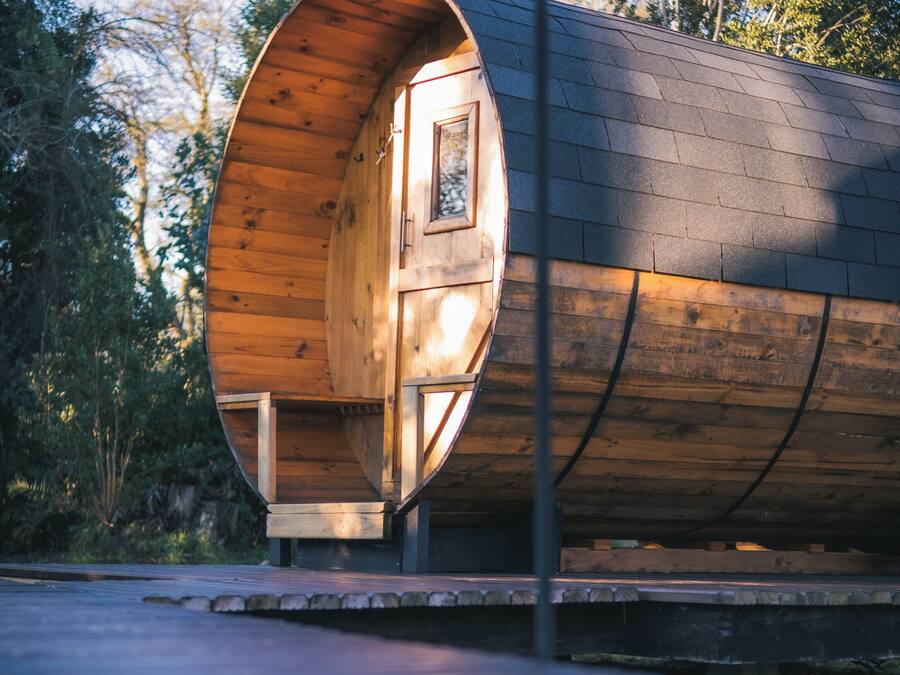 Una estructura cilíndrica de madera con una puerta y ventana, ubicada al aire libre con árboles en el fondo.