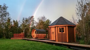Una cabaña de madera con techo inclinado, un barril y una terraza de madera.