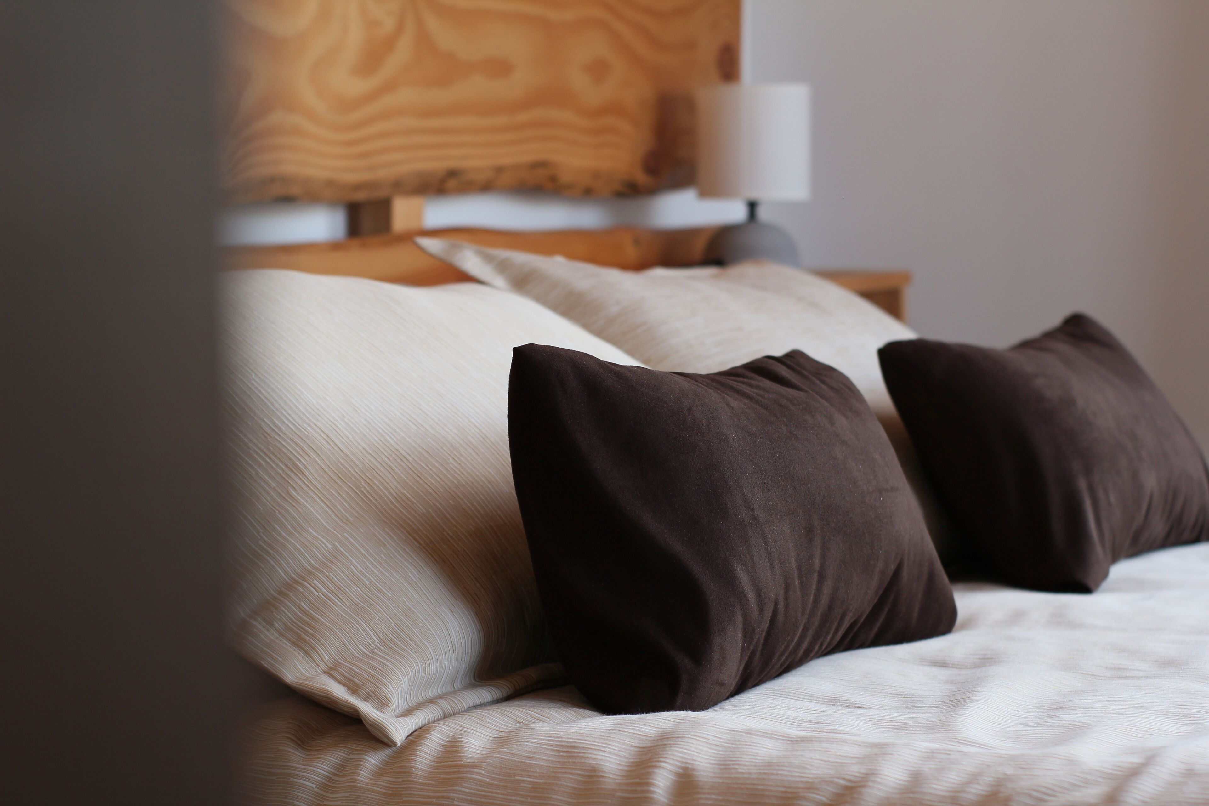 Un lit avec une tête de lit en bois, un oreiller blanc et un oreiller marron foncé.