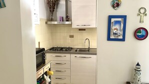 Une cuisine avec des meubles blancs, une cuisinière à gaz, un four à micro-ondes et un évier.