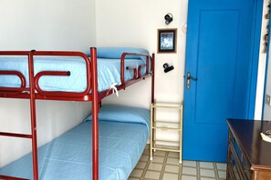 Ein Schlafraum mit Etagenbetten, einer blauen Tür, einem kleinen Regal und einem gerahmten Bild an der Wand.