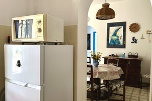 Eine Küche mit Kühlschrank, einer Mikrowelle darauf, einem Esstisch mit Stühlen und einer Kristallleuchter.