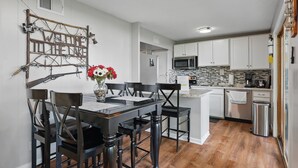 A modern kitchen with white cabinets, a microwave, and a dishwasher. There is a dining table with chairs and a vase with flowers. - EZ Access Lake House (Quinlan)