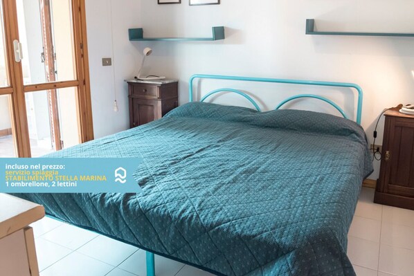 A bedroom with a bed, a nightstand, a desk, and a window with a view.