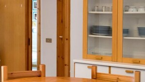 Un comedor con una mesa y sillas de madera, un armario con puertas de cristal y una puerta que da a otra habitación.