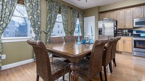 Un comedor con una mesa de madera y sillas de mimbre, una cocina con armarios de madera y electrodomésticos de acero inoxidable, y una lámpara de araña.