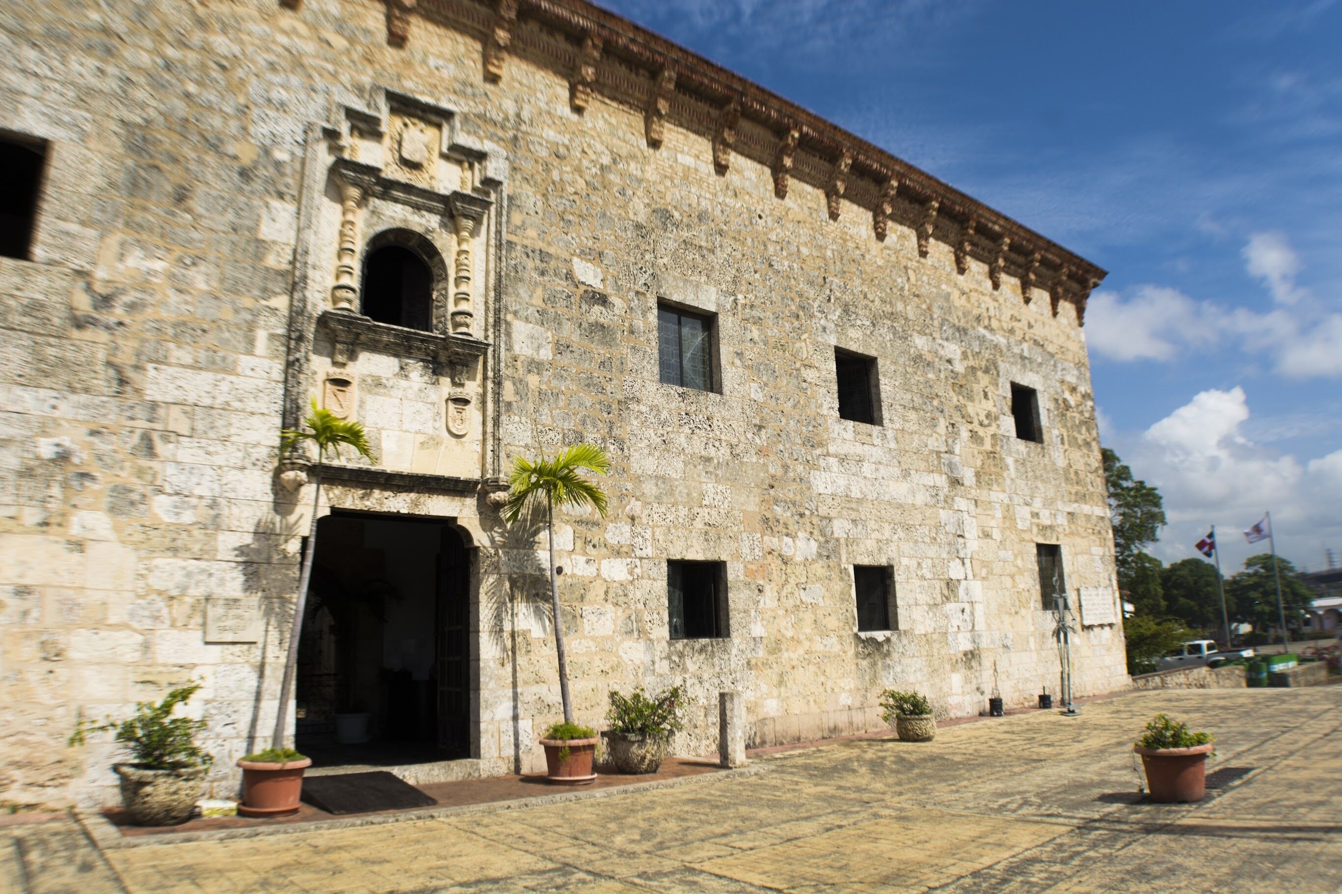 Ein historisches Steinhaus mit großem Bogenportal, zahlreichen Fenstern und Blumentöpfen.