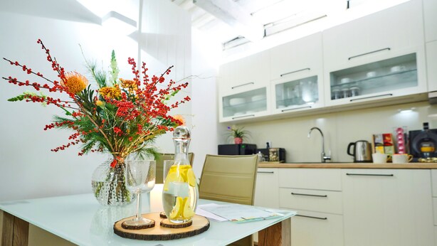 Una cucina moderna con mobili bianchi, un tavolo da pranzo con piano in vetro e un vaso con fiori e limoni.