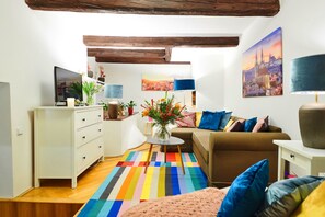 A cozy living room with a sofa, a coffee table, and a TV. There is a colorful striped rug on the floor.