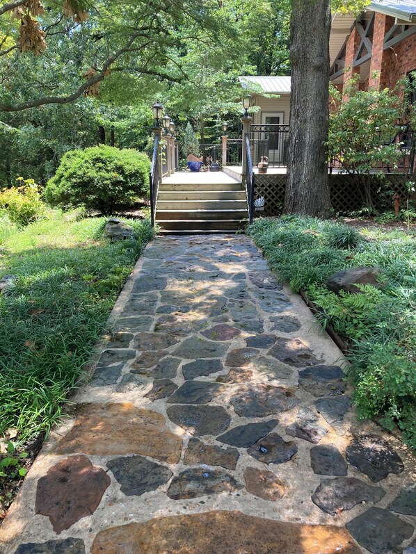 A stone pathway leading to a building with a porch and a tree. - Paw Paw Tree Estate at the foothills of Petit Jean Mt. next to Arkansas River. (Morrilton)