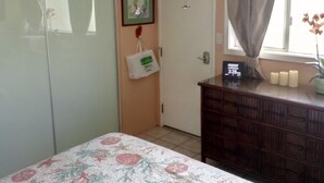 A bedroom with a bed, a dresser, a ceiling fan, a door, and a window with a curtain.