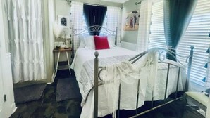 Ein Schlafzimmer mit Bett, Deckenventilator, Nachttisch, Fenster mit Vorhängen und einer Tür.