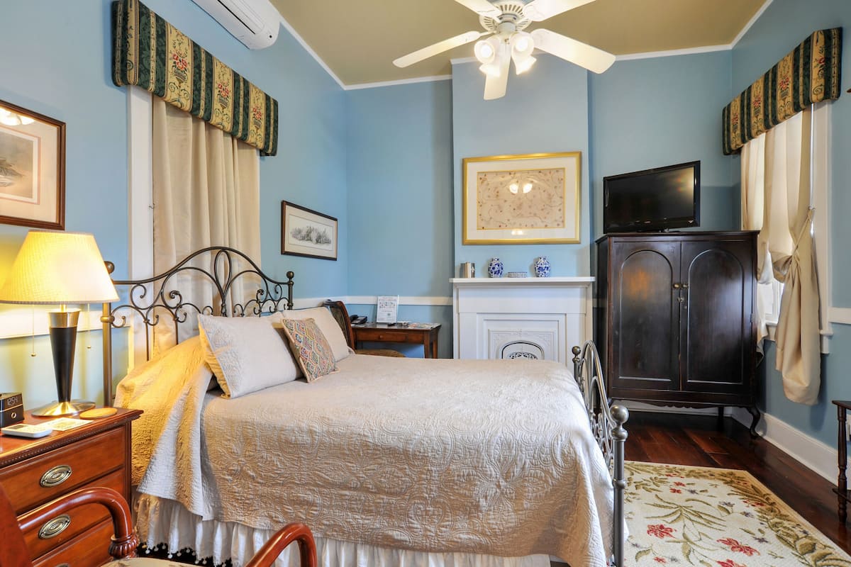 Quarto com cama, mesa de cabeceira, luminária, cômoda, televisão, armário e lareira.