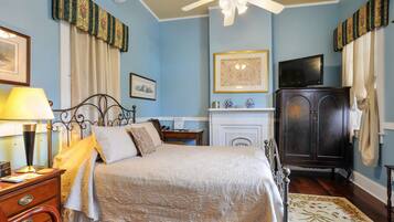 A bedroom with a bed, a nightstand, a lamp, a dresser, a television, a cabinet, and a fireplace.