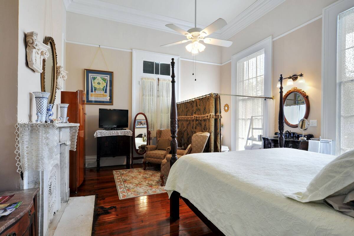 Quarto com cama de dossel, ventilador de teto, televisão e escrivaninha com cadeira.
