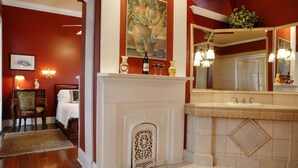 A bathroom with a white fireplace, a large mirror, and a sink with two faucets. - Ashton's Bed and Breakfast (New Orleans)