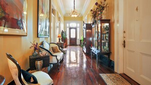 A hallway with a wooden floor, a chandelier, a sofa, and a cabinet with glass doors. - Ashton's Bed and Breakfast (New Orleans)