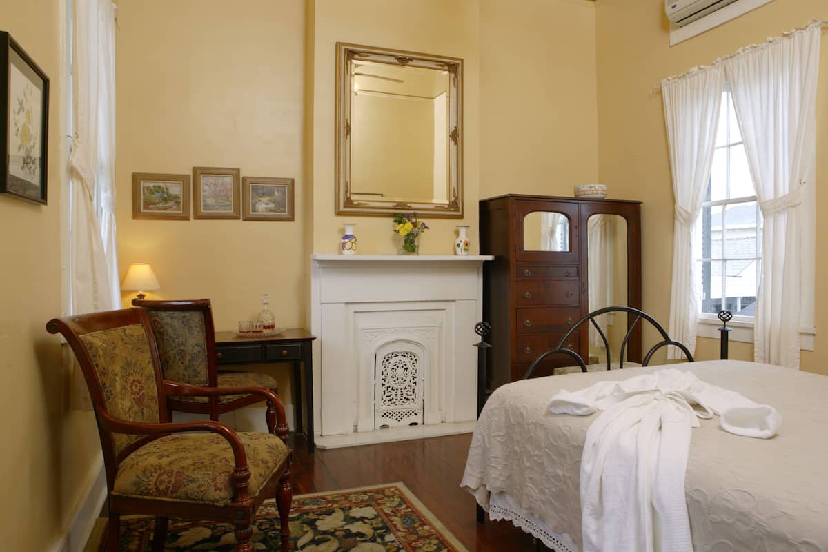 Quarto com cama, poltrona, cômoda, espelho e lareira.