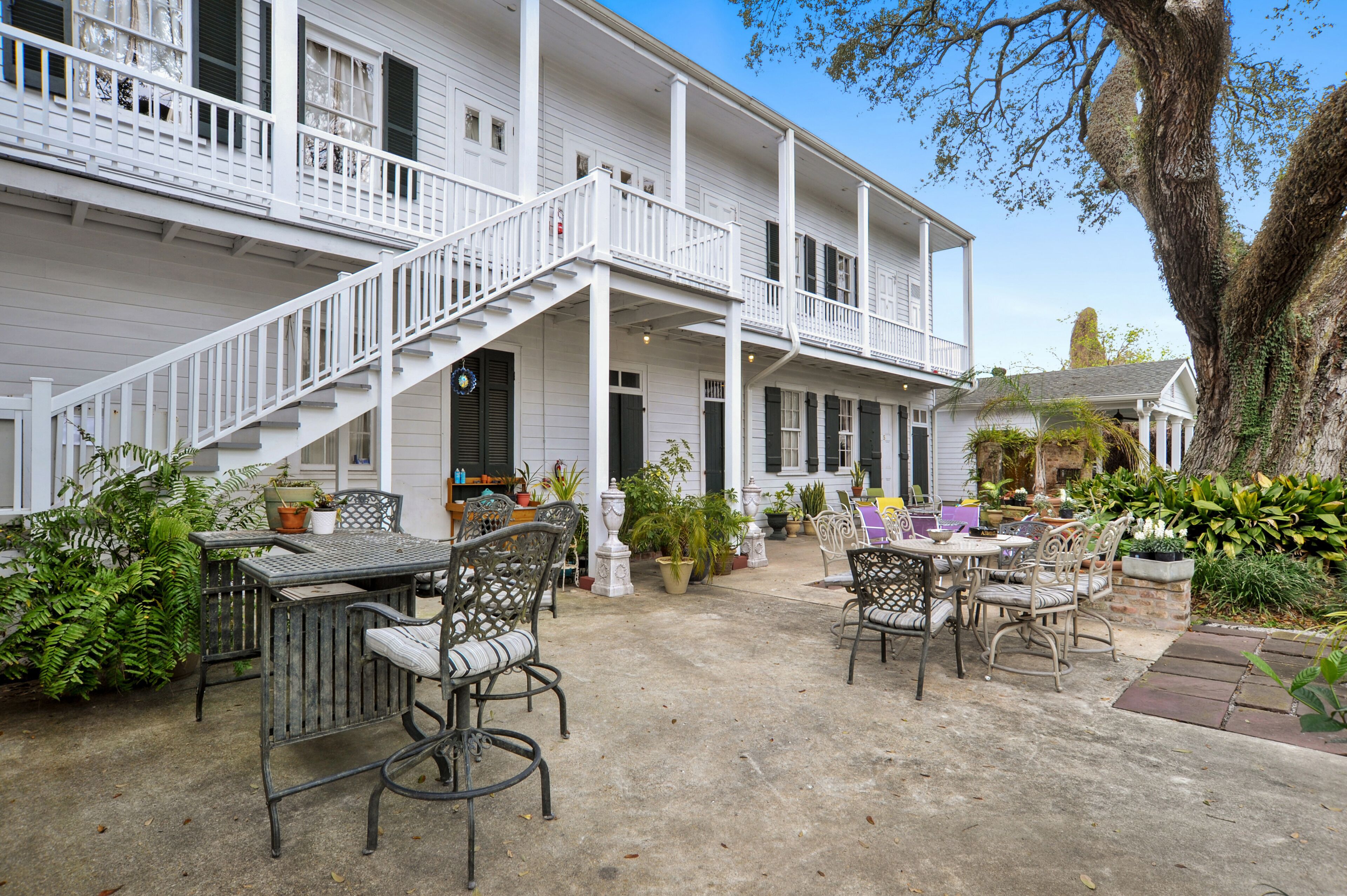 A two-story white building with a covered patio area featuring outdoor furniture and potted plants.