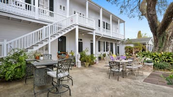 A two-story white building with a covered patio area featuring outdoor furniture and potted plants.