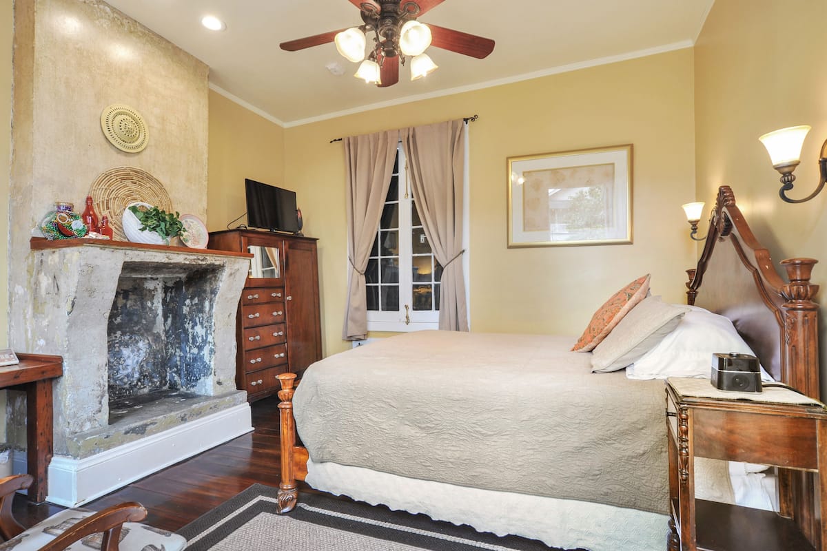 Quarto com lareira, cama com almofadas, penteadeira de madeira e ventoinha no teto.