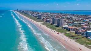 An aerial view of a coastal city with a long beach, high-rise buildings, and a clear blue sky. - Southern Destination: Bask longer, save 10% on stays of 7+ nights! (South Padre Island)