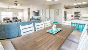 A spacious living room with a wooden dining table, blue sofas, and white chairs. - Southern Destination: Bask longer, save 10% on stays of 7+ nights! (South Padre Island)