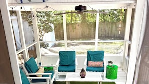 A covered outdoor seating area with white furniture, green cushions, and a small table with a decorative item.