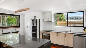 Cuina moderna amb una illa gran, electrodomèstics d'acer inoxidable i vista a una zona residencial.