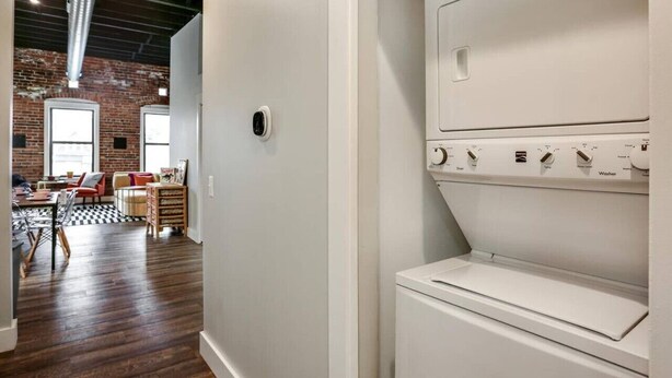 A laundry room with a white washing machine and dryer, a brick wall, and a wooden floor.
