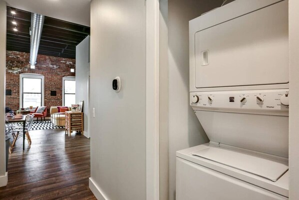 A laundry room with a white washing machine and dryer, a brick wall, and a wooden floor.