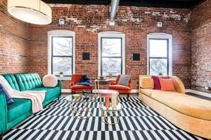 A room with a brick wall, two large windows, a green sofa, an orange sofa, and a black and white striped rug.