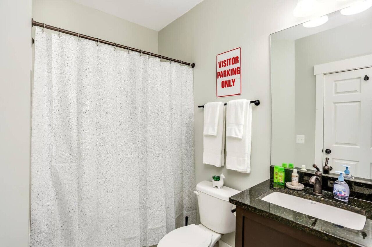 Ein Badezimmer mit Duschvorhang, Toilette, Waschbecken und Toilettenartikeln, sowie einem Schild mit der Aufschrift 'VISITOR PARKING ONLY'.