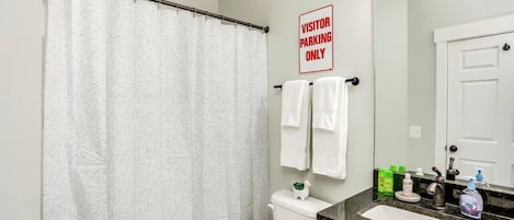 Ein Badezimmer mit Duschvorhang, Toilette, Waschbecken und Toilettenartikeln, sowie einem Schild mit der Aufschrift 'VISITOR PARKING ONLY'.