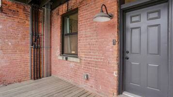 A brick building with a wooden deck, a window with a metal frame, and a dark-colored door.