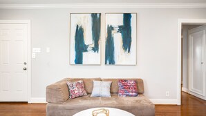 Una sala de estar con un sofá color beige, tres cojines estampados y dos cuadros abstractos en la pared.