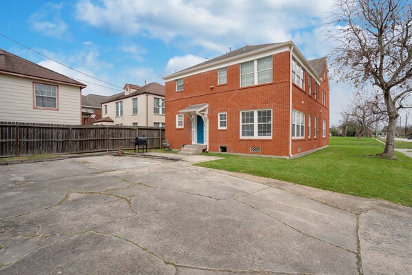 A two-story brick house with a front porch, a fenced backyard, and a tree.