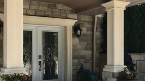A building entrance with a stone facade, white columns, and a glass door with a decorative pattern.