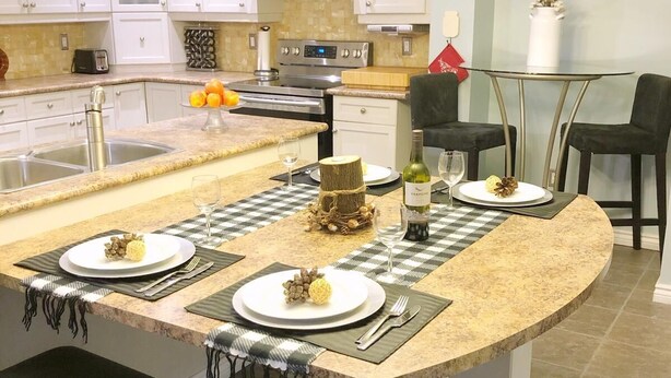 A modern kitchen with white cabinets, a central island with bar stools, stainless steel appliances, and a chandelier.