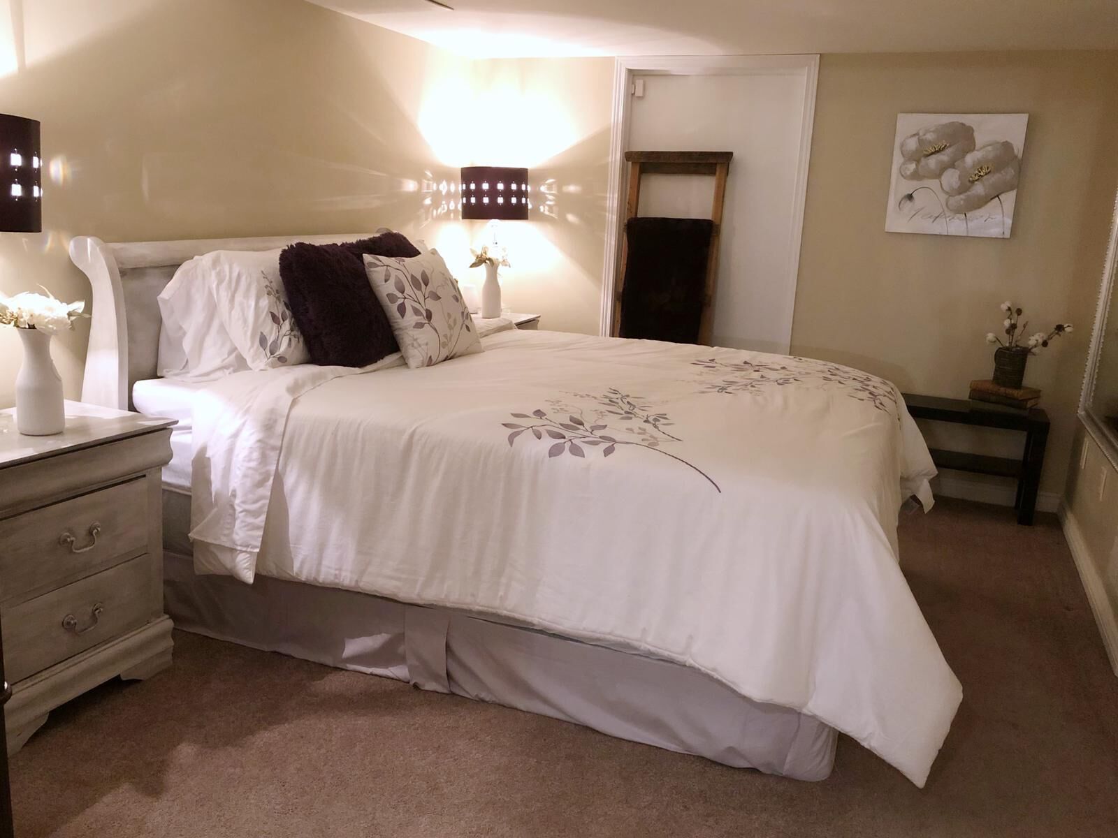 Un dormitorio ordenado con cama, mesitas de noche, cómoda y una obra de arte colgada en la pared.