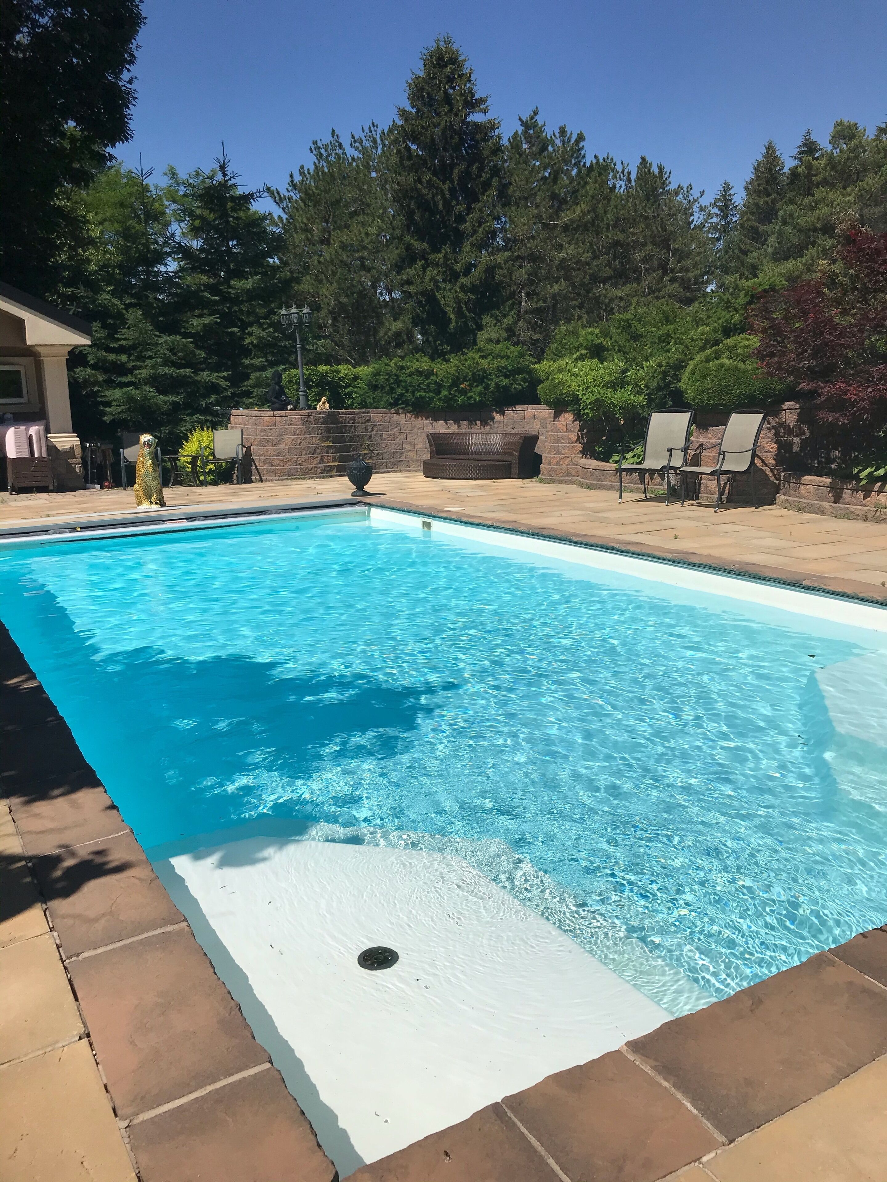 Une piscine rectangulaire à l’eau d’un bleu limpide, entourée d’une terrasse en pierre et d’un mur en pierre.