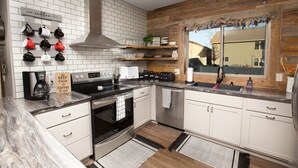Cocina con armarios blancos, campana extractora de acero inoxidable, espacio para café y ventana con vista a una casa.
