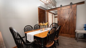 Un comedor con una mesa de madera, sillas negras y una carrera de mesa blanca. Hay jarrones con flores sobre la mesa.