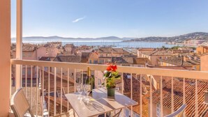 A balcony with a table, two wine glasses, and a bottle of champagne. The view includes a coastal town with buildings and a body of water. - Les Pins Dorés by Interhome (Sainte Maxime)