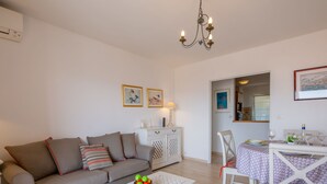 A living room with a sofa, a coffee table with fruit, a dining table with chairs, and a chandelier. - Les Pins Dorés by Interhome (Sainte Maxime)