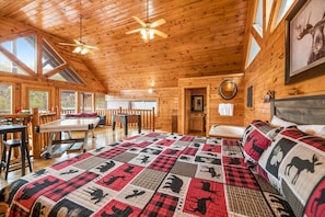 A cozy cabin interior with a large bed, wooden walls, a dining area, and a bathroom.