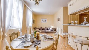 Un coin repas avec une table ronde dressée pour quatre personnes, un canapé en arrière-plan et un bar avec un comptoir et des tabourets.