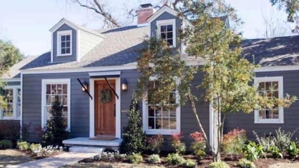Une maison à deux étages avec un porche à l’avant, une cheminée et un petit jardin où poussent différentes plantes.
